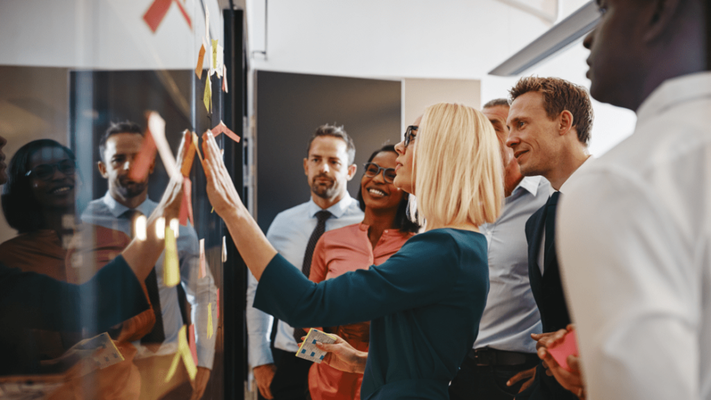 Technology leader standing with IT team writing notes on large planning wall.